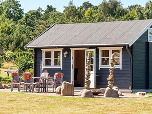 A small cabin with a dark exterior, a sloped roof, and a front porch with chairs and a table. - 10 Person Holiday Home in Farevejle (Faarevejle)