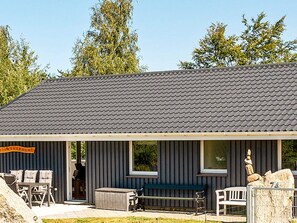 A building with a dark roof, a covered porch with chairs, and a large rock sculpture. - 10 Person Holiday Home in Farevejle (Faarevejle)