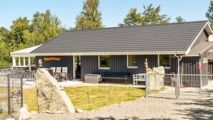 A building with a covered porch, outdoor seating, and a fenced area with rocks. - 10 Person Holiday Home in Farevejle (Faarevejle)