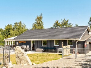 A building with a covered porch, outdoor seating, and a fenced area with rocks. - 10 Person Holiday Home in Farevejle (Faarevejle)