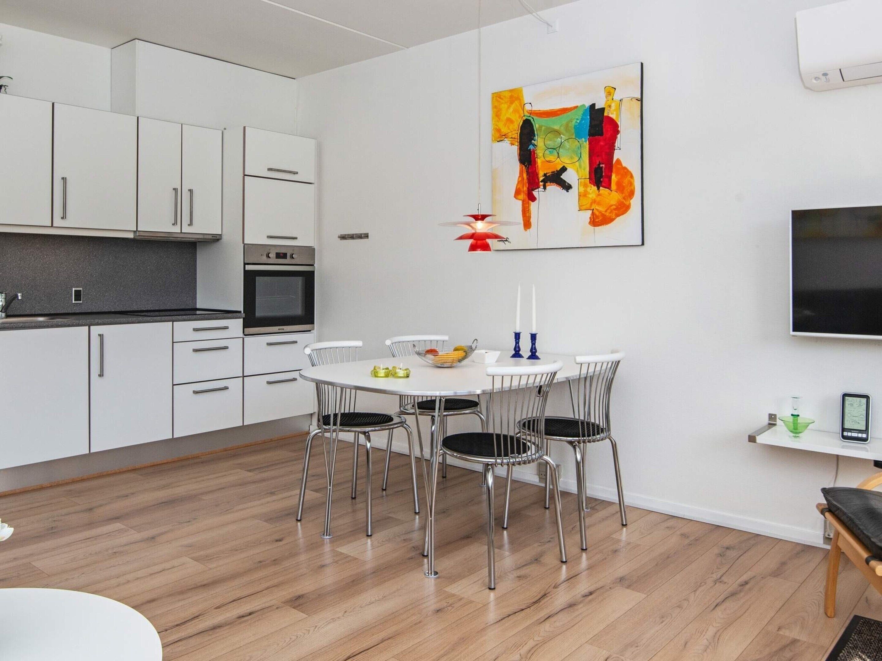A modern kitchen with white cabinets, a built-in oven, and a dining area with a round table and chairs.