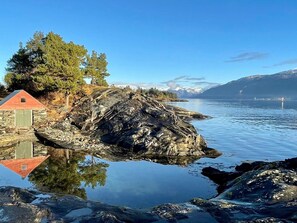 A serene lakeside scene with a stone building, a wooden dock, and a clear view of distant mountains.