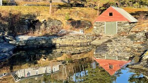 A stone house with a red roof near a body of water, surrounded by trees and a stone wall. - 6 Person Holiday Home in Hatlestrand-by Traum (Kvinnherad)
