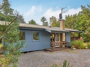 A small, single-story cabin with a chimney, a porch, and a gravel driveway.