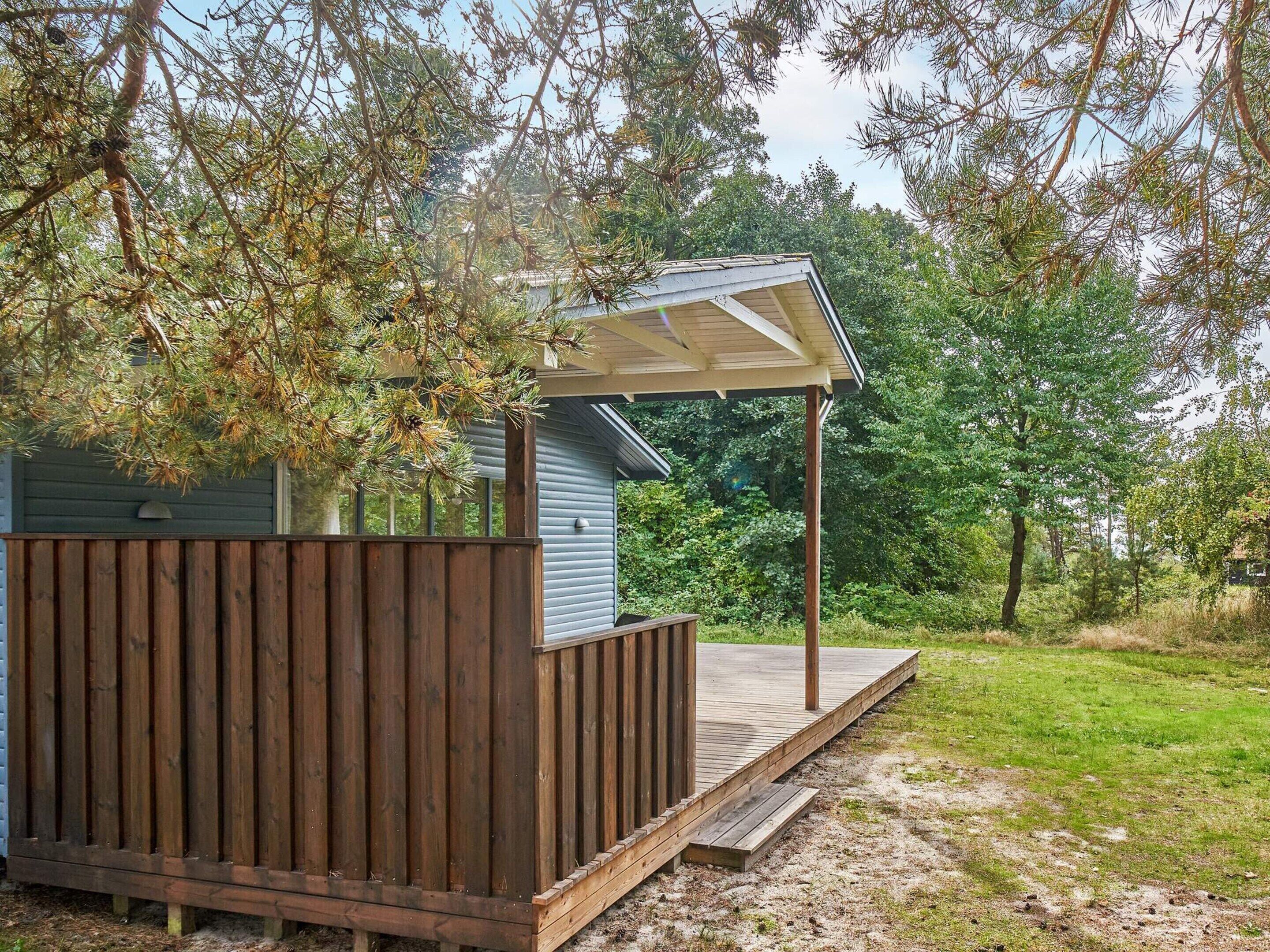 Une terrasse en bois dotée d’un espace abrité, entourée d’arbres et d’une pelouse.