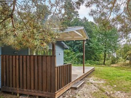 Una terraza de madera con un área techada, rodeada de árboles y césped.