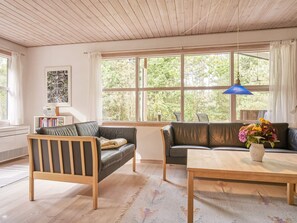 A living room with a wooden ceiling, a sofa, a chair, a table, and a window with a view of trees.