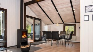 A modern interior with a wood-burning stove, a dining area with chairs, and a view through large windows. - 6 Person Holiday Home in Oksbol-by Traum (Oksbol)