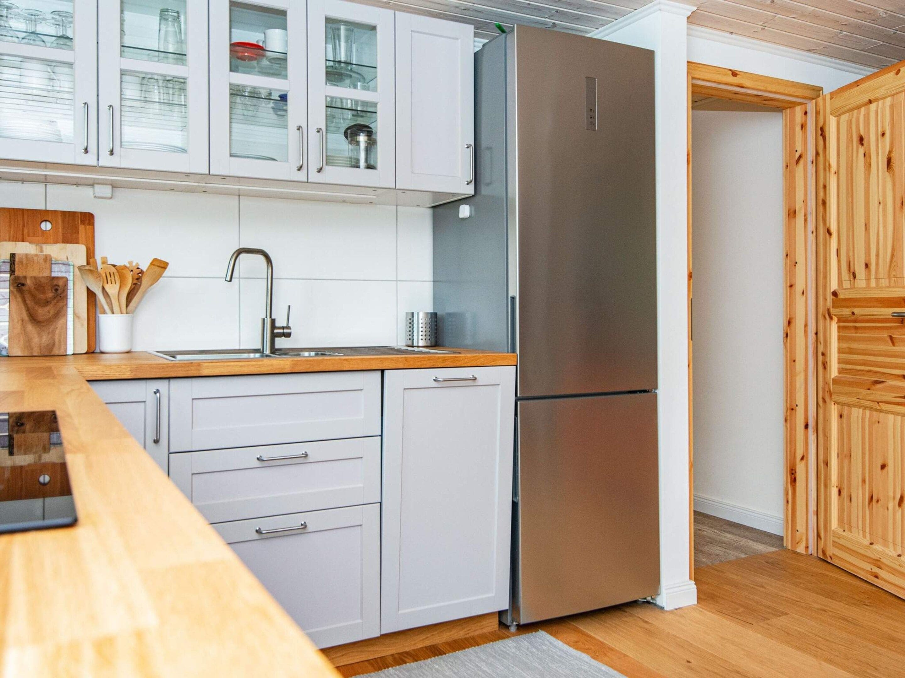 Una cocina con armarios blancos, un refrigerador de acero inoxidable, una encimera de madera y un lavamanos con un grifo moderno.