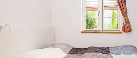 A single-bed room with a wooden ceiling, a window with a view of greenery, and a white bedside lamp.