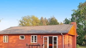 Ein rotes Ziegelhaus mit einem Ziegeldach, einer Holzterrasse und einer Glastür, die zu einem Innenraum mit einem Bett und einem Tisch führt.