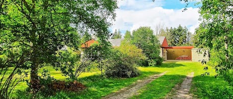 A rural landscape with a dirt path leading to a wooden structure.