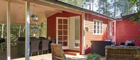 A wooden cabin with a covered porch, wicker furniture, and hanging planters.