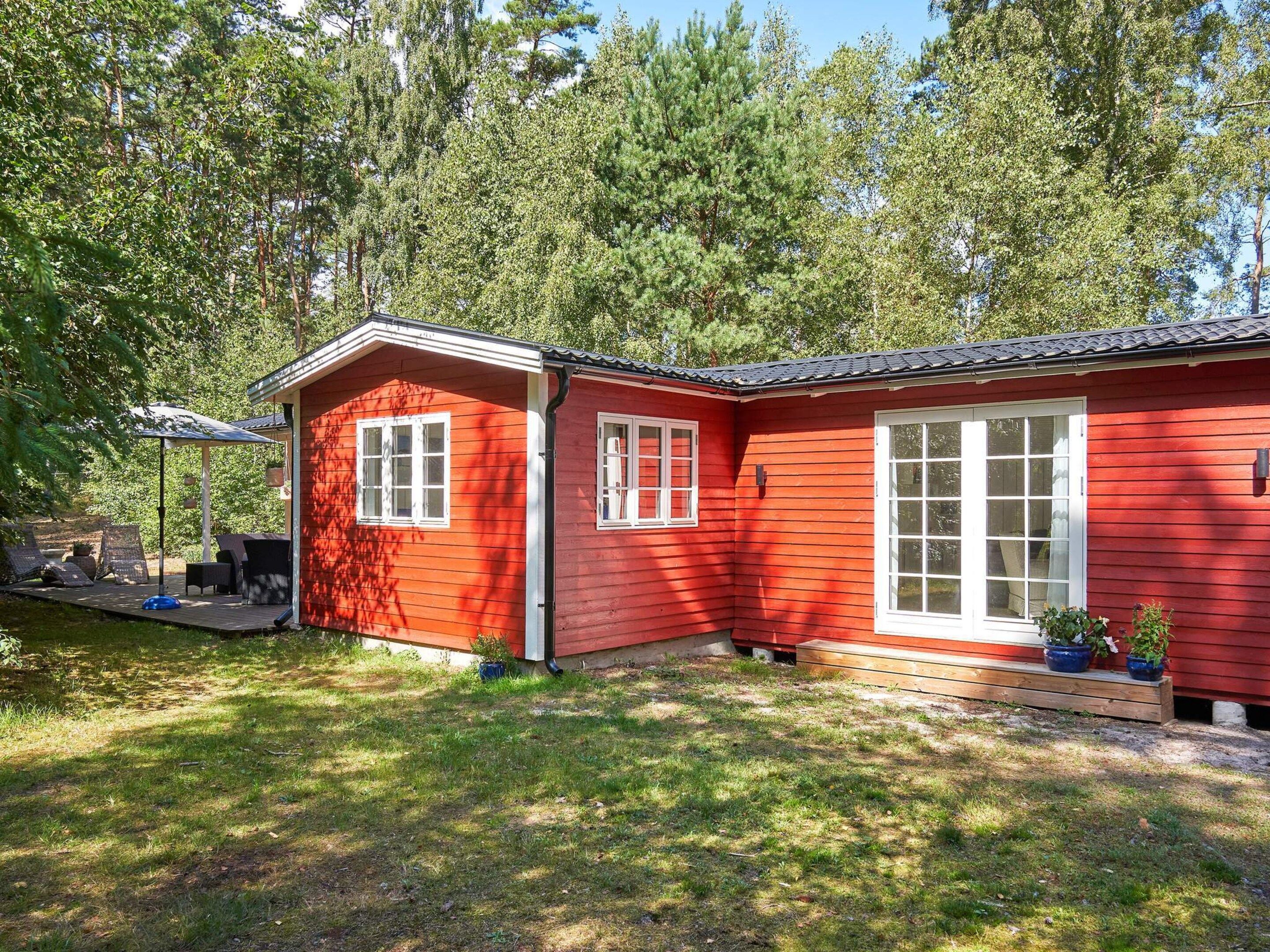 Ein rotes Holzhaus mit einer Terrasse, weißen Fenstern und Blumentöpfen.