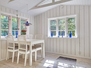 A dining area with a white table and chairs, a hanging pendant light, and a window with blue bottles on the sill. - 4 Star Holiday Home in Aakirkeby (Akirkeby)
