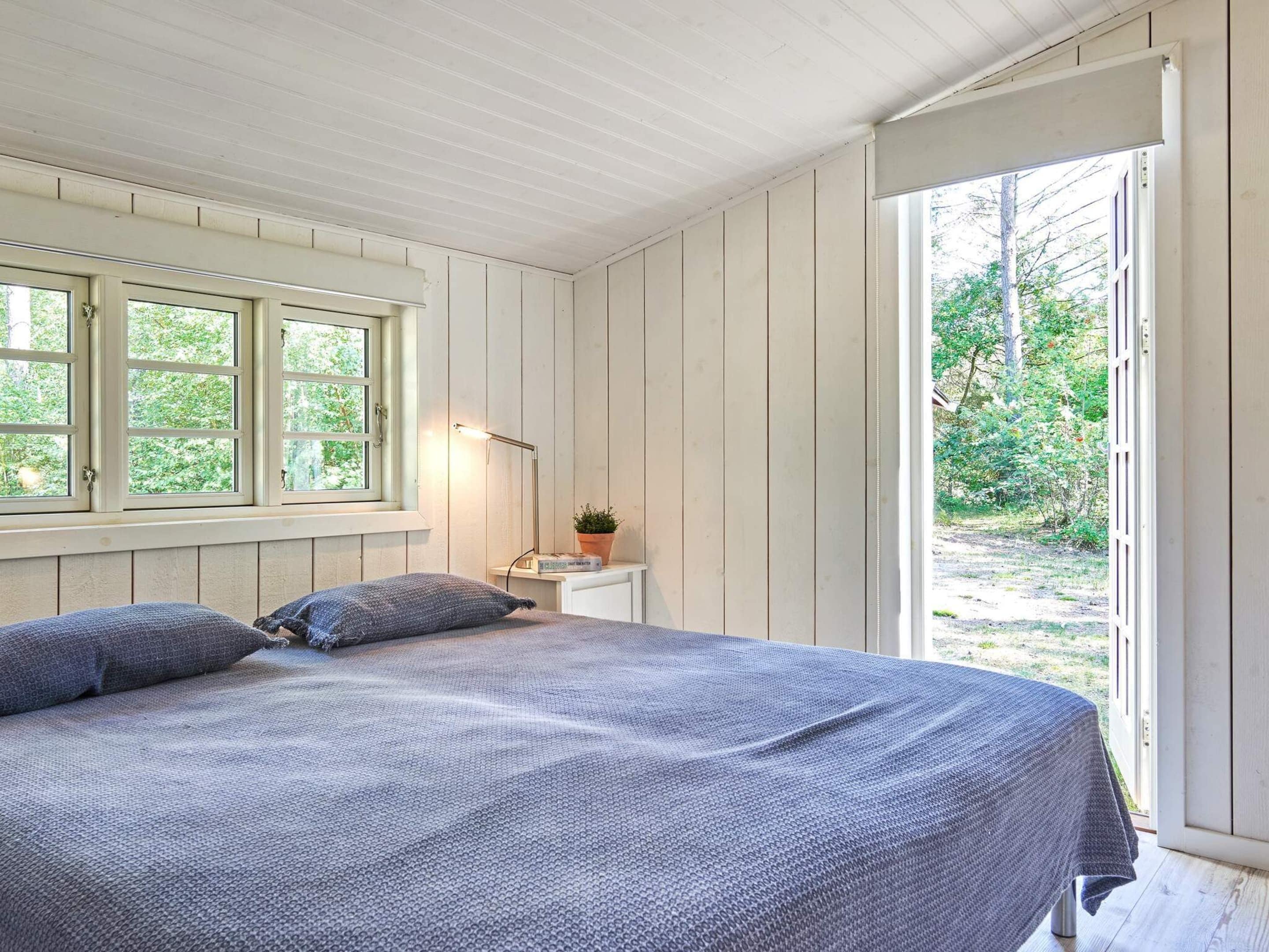 A bedroom with a bed, a nightstand, a lamp, and a window.