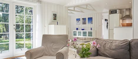 A spacious living room with a checkered armchair, a grey sofa, and a glass coffee table with a vase of flowers.