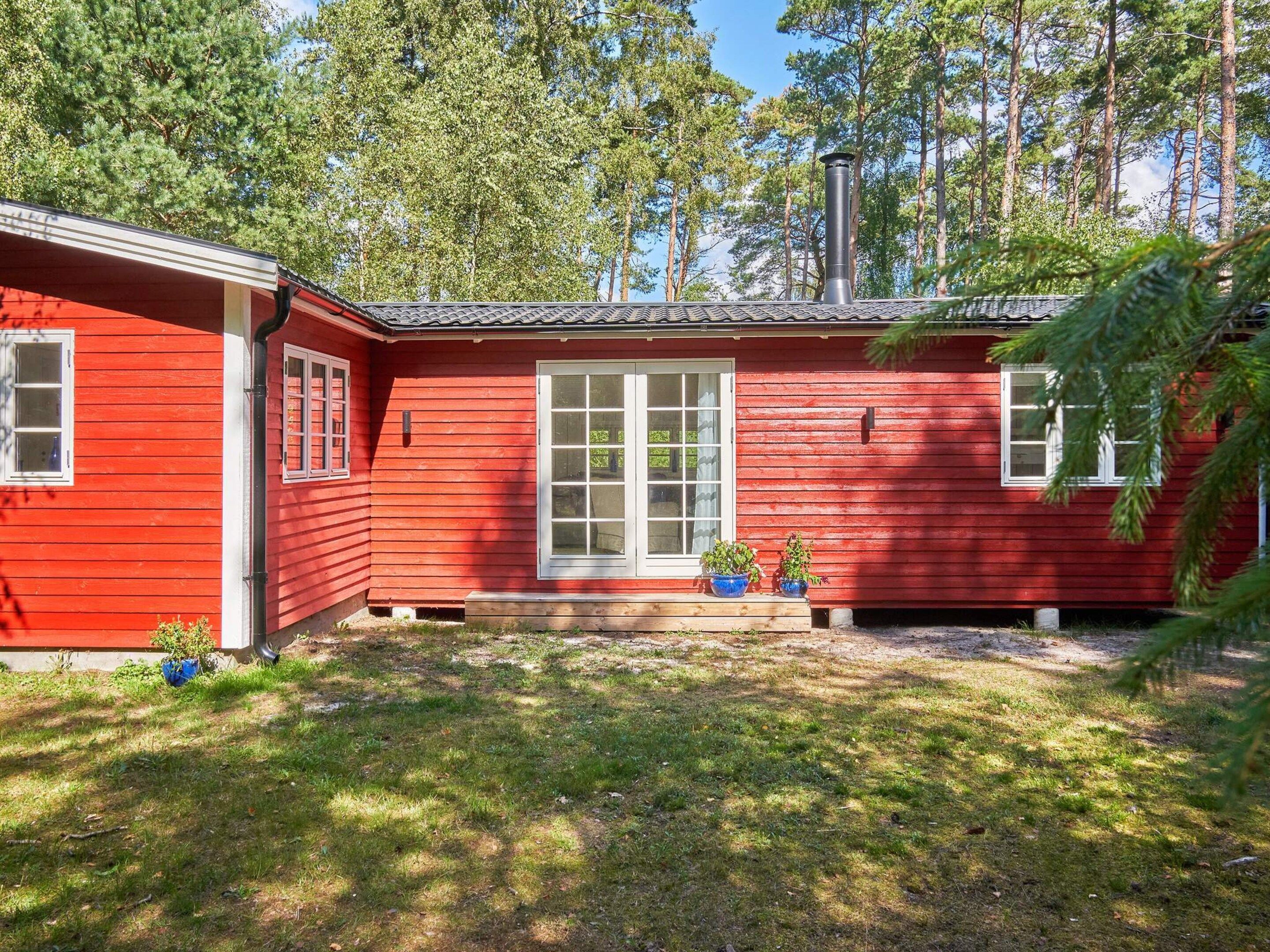 A red wooden house with a white door and windows, surrounded by a grassy yard and trees.