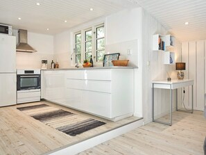 A modern kitchen with white cabinetry, a built-in oven, a stainless steel range hood, and a window providing natural light.
