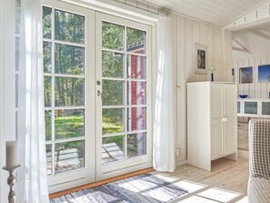 A room with a large sliding glass door leading to a garden, a white cabinet, and a checkered chair.