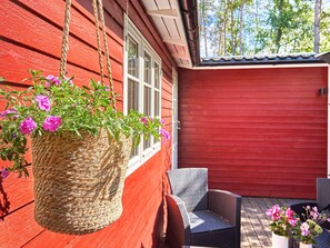 A red wooden building with a hanging basket of flowers and a wicker chair outside.