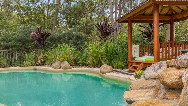 A swimming pool with a wooden deck and lounge area, surrounded by rocks and lush greenery. - Stylish rural retreat on the foothills of Mt. Mee (Moorina)