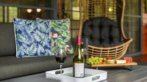 A cozy seating area with a sofa, a wicker chair, and a tray with a bottle of wine, glasses, and a selection of fruits and cheeses. - Stylish rural retreat on the foothills of Mt. Mee (Moorina)
