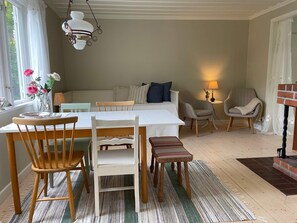 Un coin repas comprenant une table, des chaises, un luminaire suspendu et donnant sur une chambre avec un lit et un fauteuil.