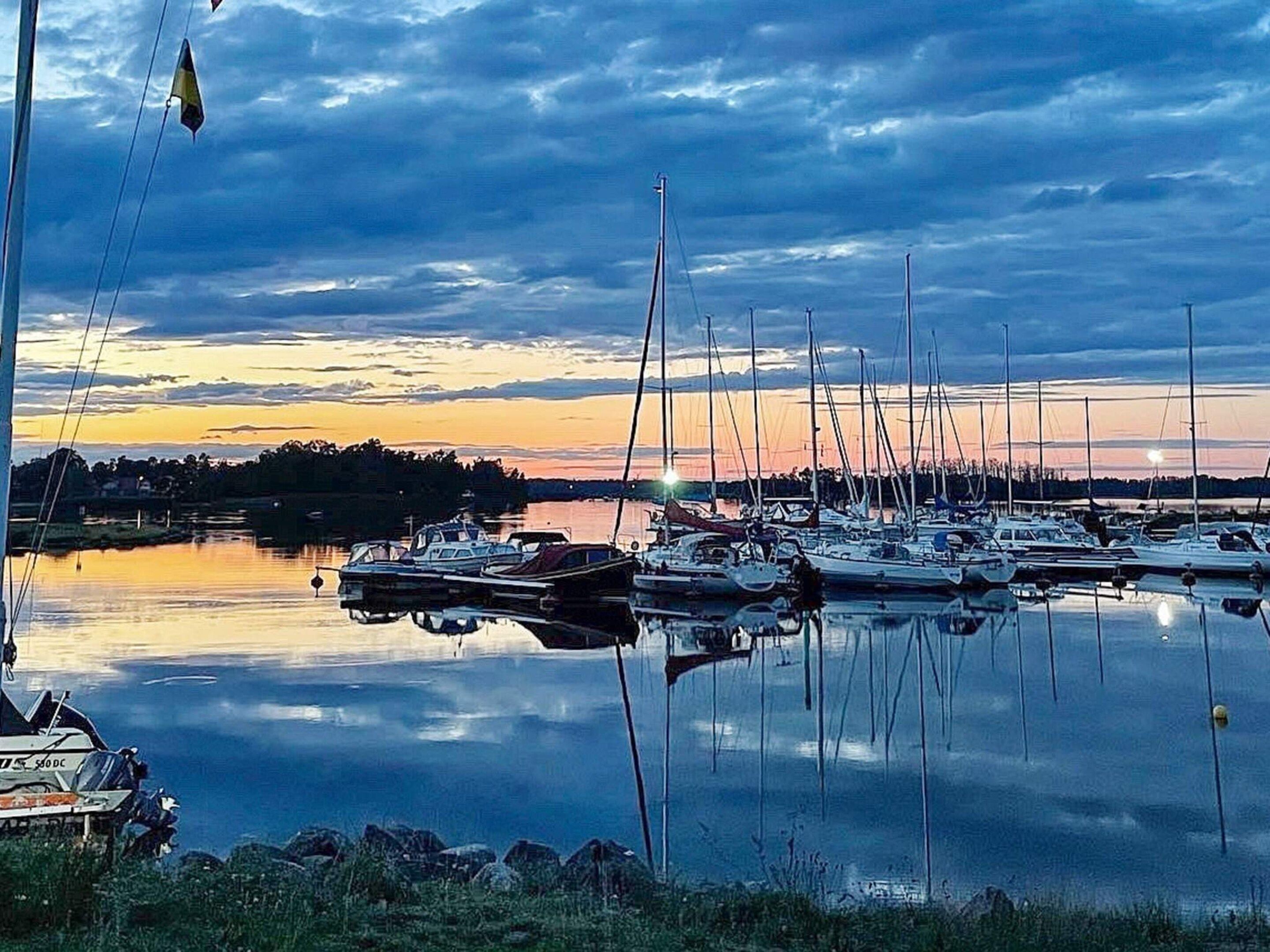A marina with multiple boats docked, calm water, and a sunset in the background.