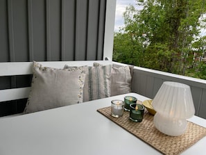 Un balcón con una mesa blanca, un camino de mesa tejido, velas y una lámpara.