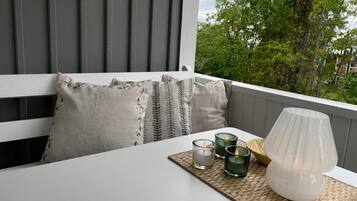 Un balcón con una mesa blanca, un mantel tejido, velas y una lámpara.