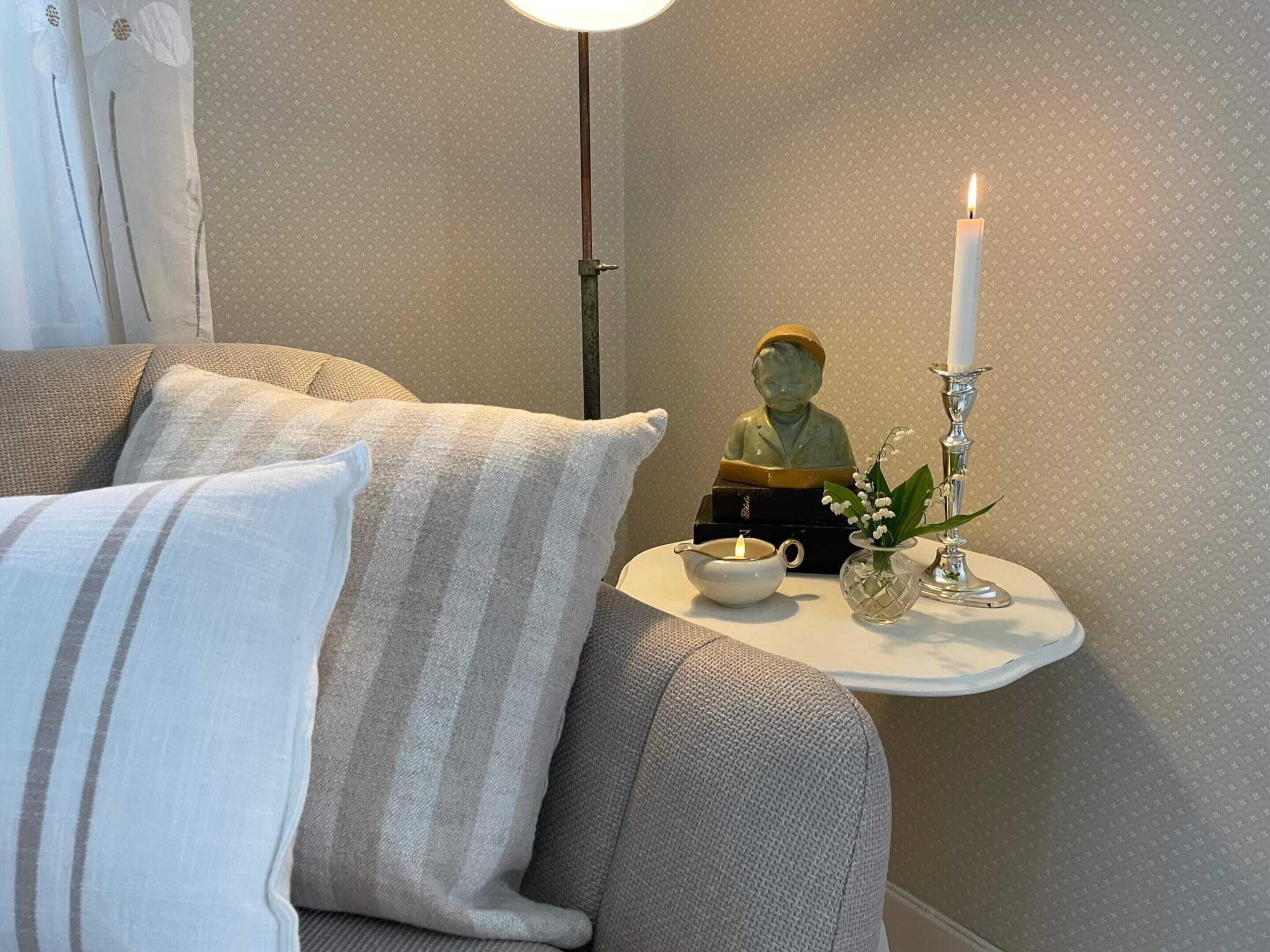 A cozy corner with a sofa, a small table, a statue, a candle, and a vase with flowers.
