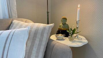 A cozy corner with a sofa, a small table, a statue, a candle, and a vase with flowers.