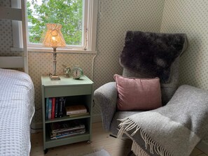 A cozy room with a bookshelf, a lamp, a chair with a blanket, and a window with a view of trees. - 4 Person Holiday Home in 38472 (Timmernabben)