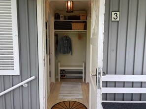 Un couloir étroit mène à une pièce dont la porte est marquée du numéro « 3 ». On y trouve un porte-chaussures, une veste suspendue et des étagères avec des paniers et une lanterne.
