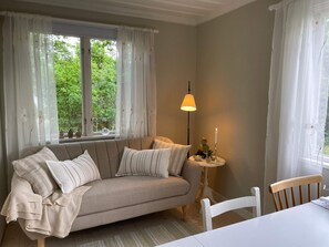 Una habitación acogedora con un sofá, una mesa y una silla. Hay una ventana con cortinas, una lámpara y una vela sobre la mesa.