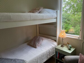 Ein Schlafraum mit Etagenbett, Ausblick aus dem Fenster, Nachttischlampe und kleinem Bücherregal.