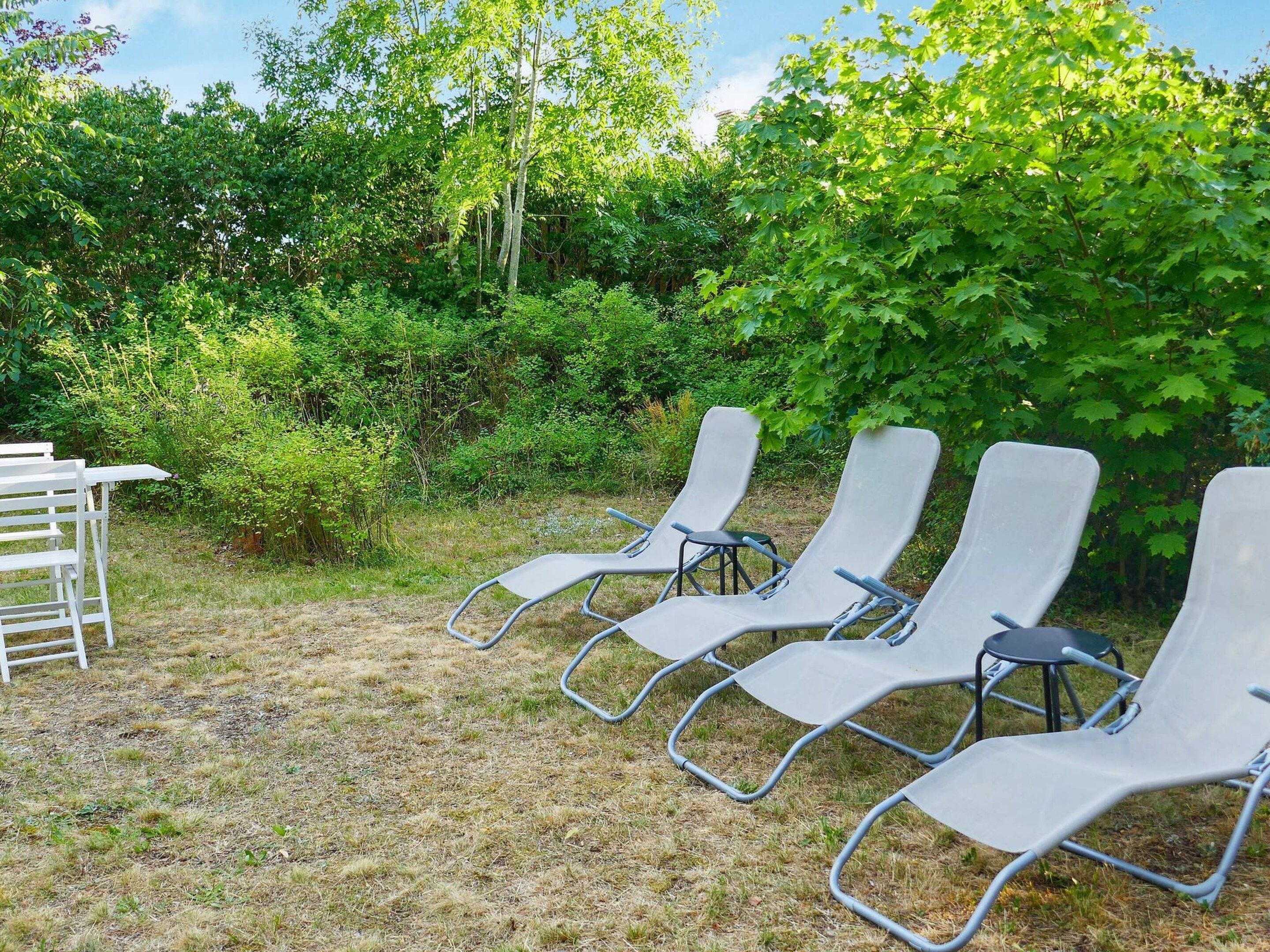 Outdoor lounge chairs arranged in a row, surrounded by dense greenery and trees.