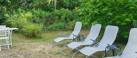 Outdoor lounge chairs arranged in a row, surrounded by dense greenery and trees.