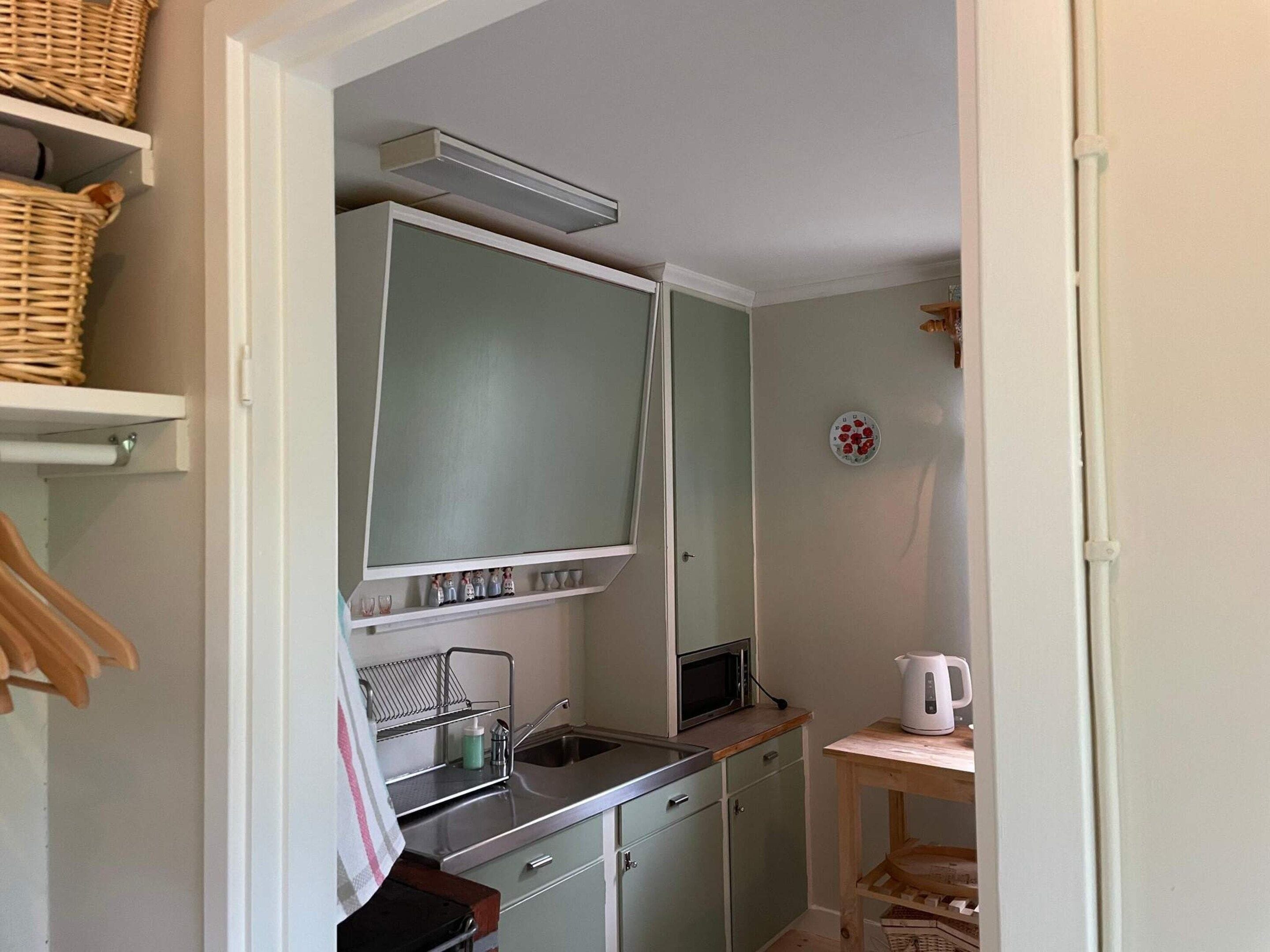 Una cocina compacta con microondas, lavamanos y una pequeña mesa con hervidor.