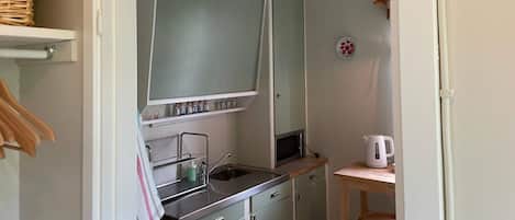 A compact kitchen with a microwave, sink, and a small table with a kettle.