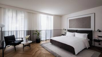 Habitació d'hotel moderna amb un llit gran, una taula rodona petita, una cadira i una planta en test.