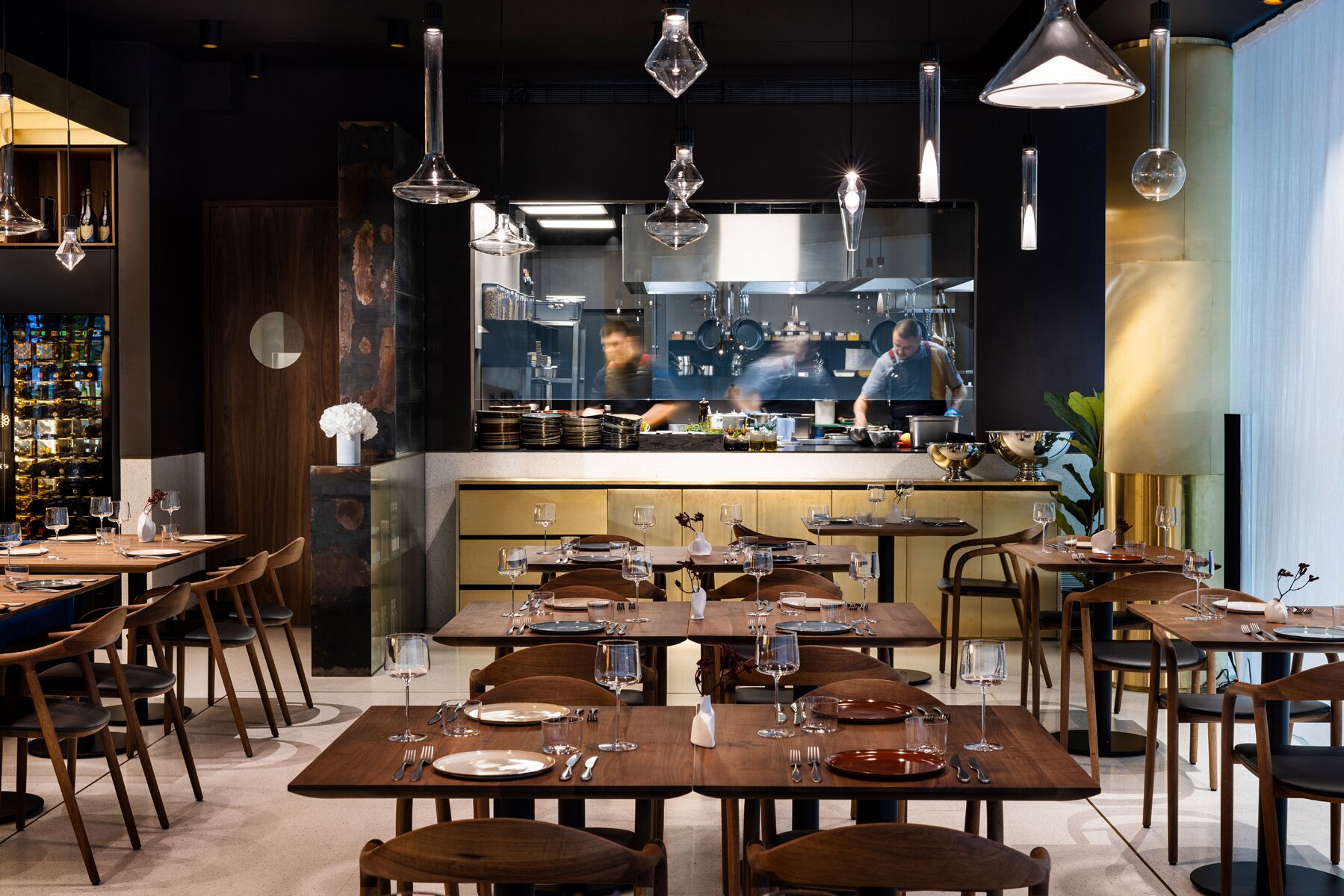 A restaurant interior with multiple dining tables, chairs, and hanging pendant lights.