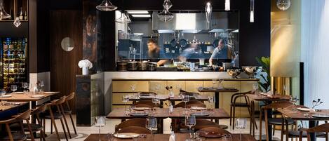 A restaurant interior with multiple dining tables, chairs, and hanging pendant lights.