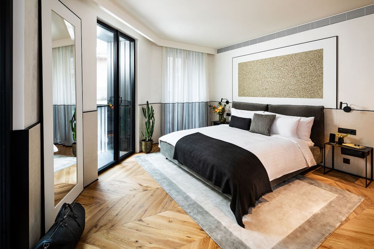 Quarto de hotel moderno com uma cama grande, porta de correr de vidro para uma varanda e decoração minimalista.