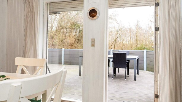 A room with a white ceiling, a door leading to an outdoor patio, a white table with a chair, and a black chair. - 5 Person Holiday Home in Thyholm (Thyholm)