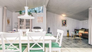 A spacious room with a dining area featuring white chairs and a table, a sofa, and a television. - 5 Person Holiday Home in Thyholm (Thyholm)