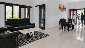 Een moderne woonkamer met een zwarte leren bank, een glazen salontafel en een plafondventilator.