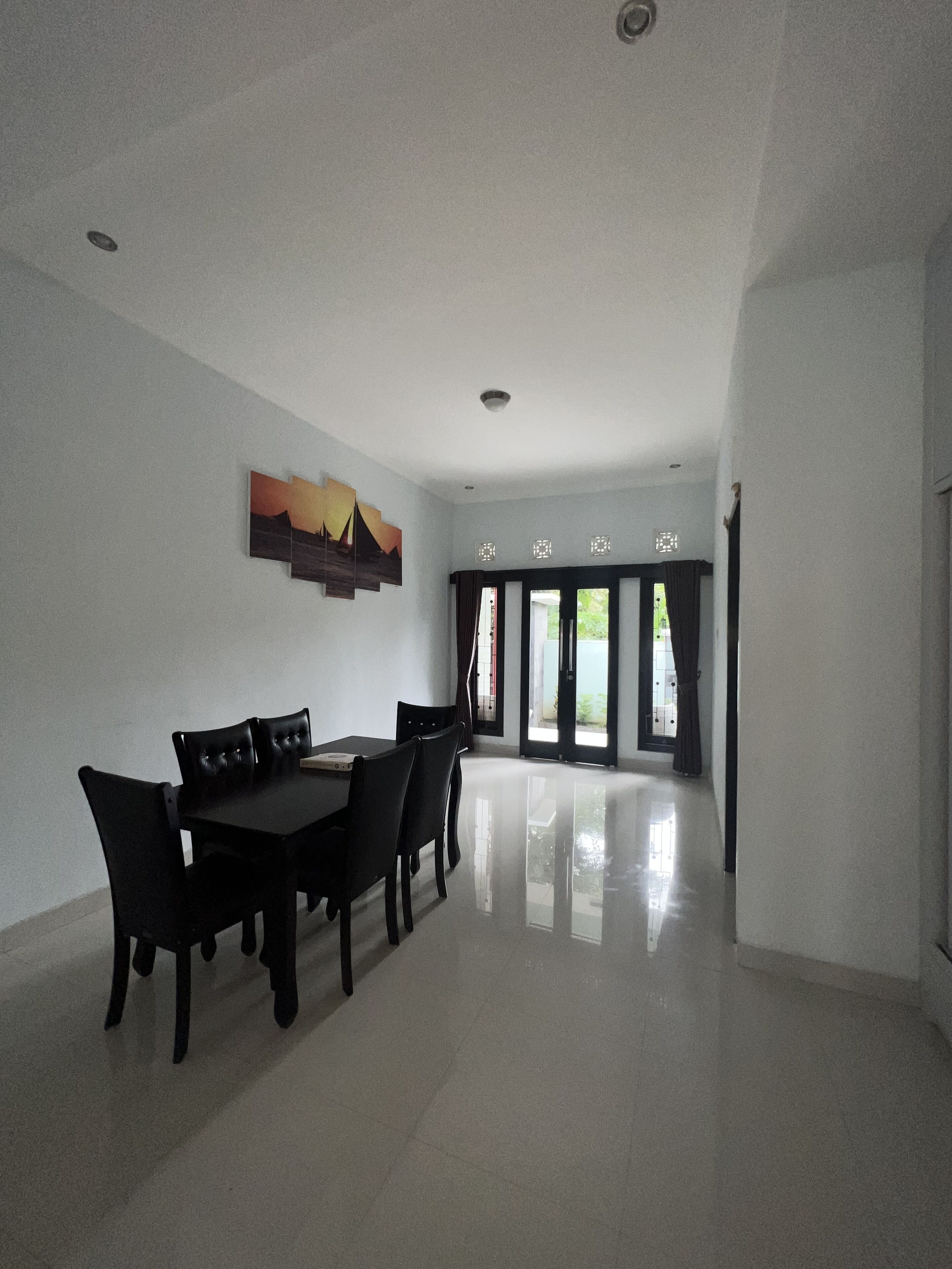 A spacious dining area with a black table and chairs, a ceiling light, and a view through a glass door to an outdoor area.