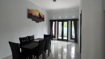 A spacious dining area with a black table and chairs, a ceiling light, and a view through a glass door to an outdoor area.